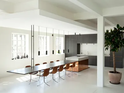 A modern minimalist kitchen with a concrete floor, long dining table, and dark cabinets.