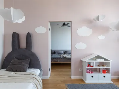 Children's bedroom featuring pink walls with white paper clouds, a bed with a bunny-shaped headboard, and a small white dollh