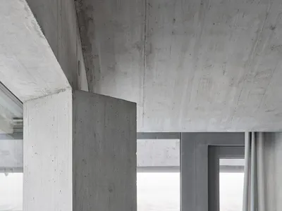 A minimalist concrete living room with exposed concrete surfaces, large windows, and simple furniture.