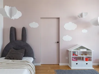 A modern children's bedroom with a fabric headboard designed like bunny ears, white clouds hanging from the ceiling, and a sm