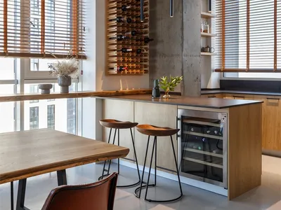 A modern kitchen featuring a wooden wine rack and bar stools, with natural light streaming in through the large windows.