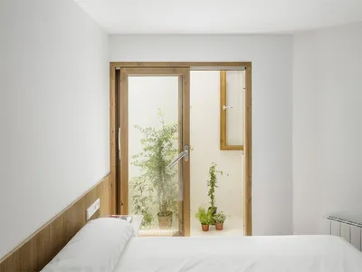 Modern minimalist bedroom with white walls, wooden headboard, and potted plants.