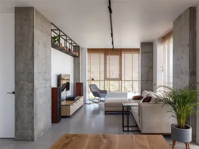 Modern, minimalist living room with concrete walls and floor, white couch, and floor-to-ceiling windows.