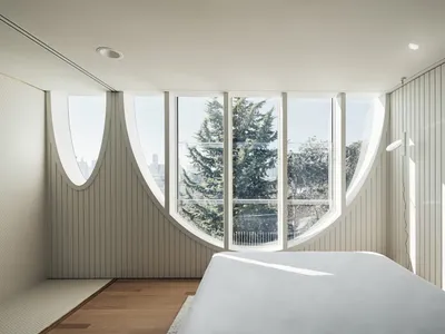 A modern bedroom featuring a large oval window with a view of trees and a city skyline.