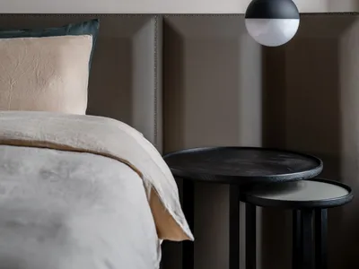 Modern minimalist bedroom with a neatly made bed featuring light-colored bedding, a hanging light fixture, and fabric-paneled
