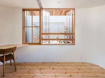 A minimalist living room featuring wooden flooring and a large window with a wooden frame.