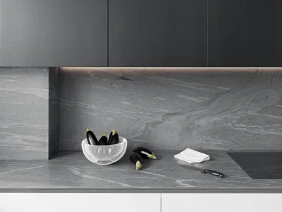 A modern minimalist kitchen with a black stone countertop featuring a bowl of eggplants, a knife, and a white napkin.