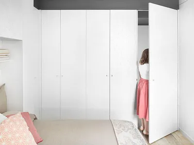 A minimalist bedroom with white paneling on the walls and a bed with a beige cushion and pink throw pillow.