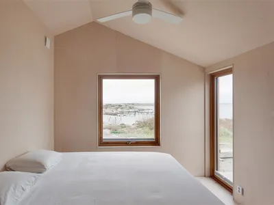 A minimalist bedroom with a window overlooking a coastal landscape.