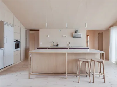 A minimalist residential kitchen featuring a wooden island and stools, surrounded by soft lighting and clean lines.
