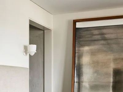 A minimalist bedroom with textured blue bedding and a neutral headboard against a white wall, featuring a large mirror with a