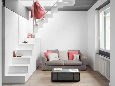 A minimalist living room featuring white concrete stairs, a gray sofa with coral and white pillows, and a metallic coffee tab