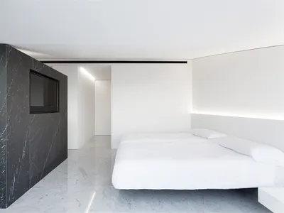 A minimalist bedroom with white walls, black marble accents, and two white beds.