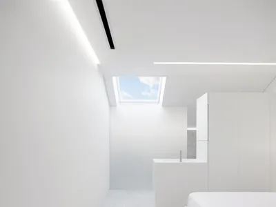 Modern, minimalist bedroom with white walls, ceiling, and floor. Features a large window with natural light.