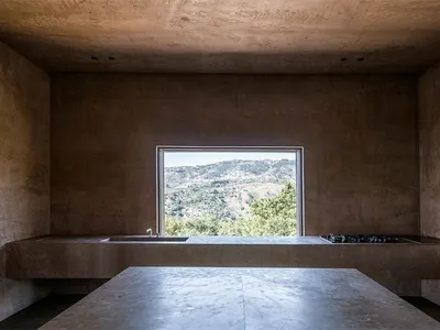 極簡風格的廚房，配有混凝土檯面與大型窗戶，窗外可見山巒與樹木景觀。