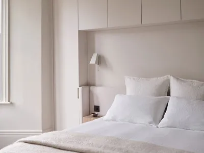 A minimalist bedroom with muted tones and soft textures, featuring a bed with white bedding and a light-colored headboard, si