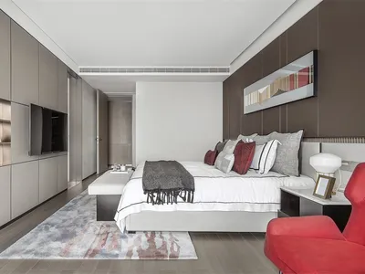 Modern minimalist bedroom with white bed, grey and red pillows, and a red accent chair, featuring gray and pink rug, white an