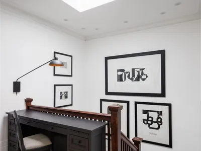 A modern home office featuring a black desk, white walls, and framed black and white photos on the wall.