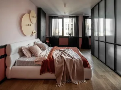 A modern bedroom with a white bed, pink and beige bedding, and wood flooring.