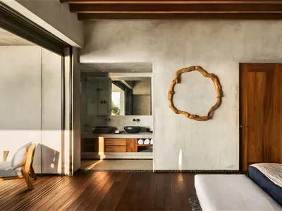 Modern minimalist bedroom with concrete walls, wooden floor, and dark bedding.