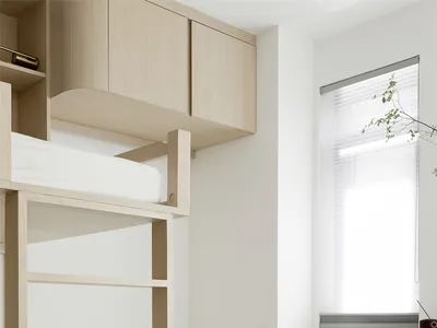 A minimalist bedroom with wooden bunk beds and a chair, featuring a white wall and wooden flooring.