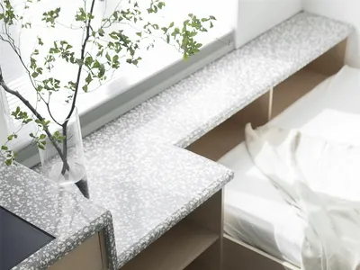A minimalist bedroom with a white bed, terrazzo desk, and wooden elements.