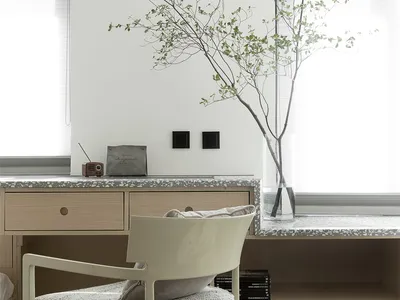 A modern home office featuring a wooden chair with a textured seat, a wooden desk with a terrazzo countertop, and a terrazzo