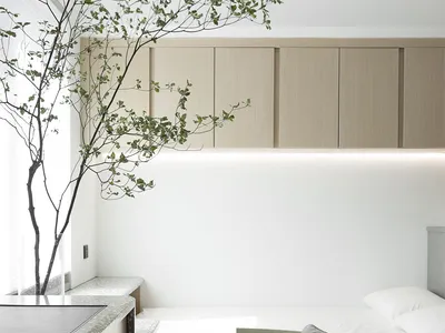 A minimalist bedroom featuring a fabric chair with a cushion, modern furniture, and a green plant.