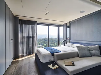 Modern minimalist bedroom with a blue bedspread, large windows, and a view of the mountains.