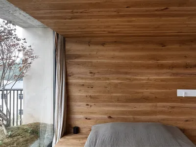 A minimalist bedroom featuring wooden walls and a bed with a grey sheet.
