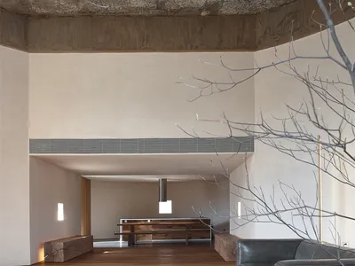 A modern industrial living room featuring exposed concrete beams, wood flooring, and minimalist furniture.