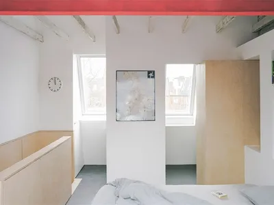 A minimalist bedroom featuring a wooden bed and wood paneling, with a clock on the wall and a painting on the floor.