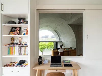A minimalist study room with a concrete wall and desk, featuring a person seated at the desk.