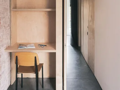 A minimalist home office featuring a wooden desk and chair, with shelves and a door for organization.