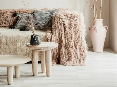 A cozy living room with a plush faux fur sofa and throw blanket, featuring minimalist decor and soft lighting.
