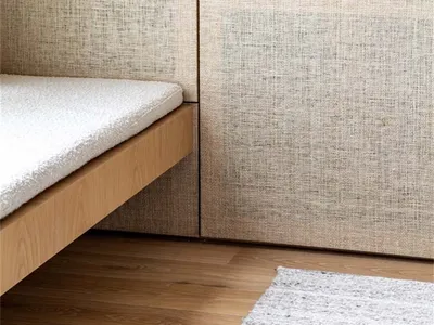 A minimalist bedroom featuring a bed with a wooden frame, backrest cushion, and wooden flooring.