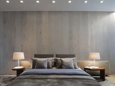 A minimalist bedroom with a wooden texture wall, grey bedding, and matching bedside tables with lamps.