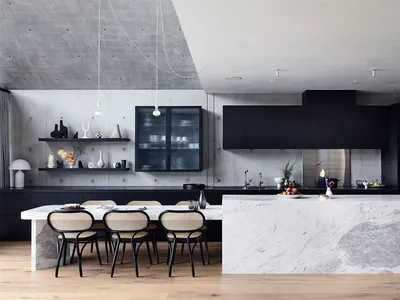 A modern minimalist kitchen featuring a white marble island, black cabinets, and concrete walls.