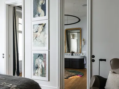A modern bedroom featuring wooden flooring and a carpet, with a door leading to a bathroom and an armchair in the foreground.