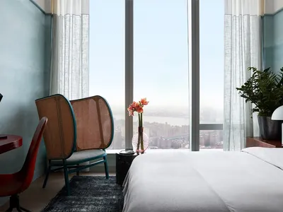 A modern minimalist hotel room with textured fabric, large windows, and a clean white bed.