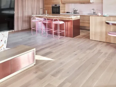 A modern kitchen featuring a wooden floor, cabinets, and island with pink stools.