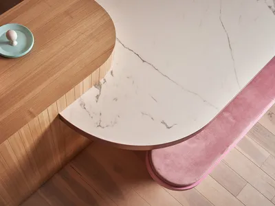 A modern interior design featuring a curved marble countertop with wooden accents and pink seating.
