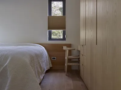 Wooden furniture and white bedding in a minimalist bedroom setting with a small window.