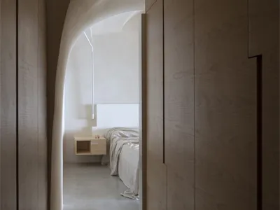 A minimalist bedroom with curved walls, white palette, and wooden furniture.
