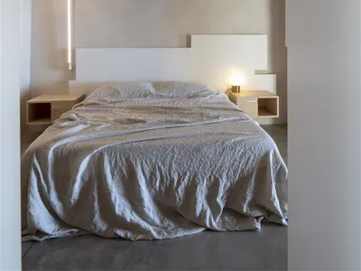 Minimalist bedroom with a concrete floor, bed, and twin bedside tables.