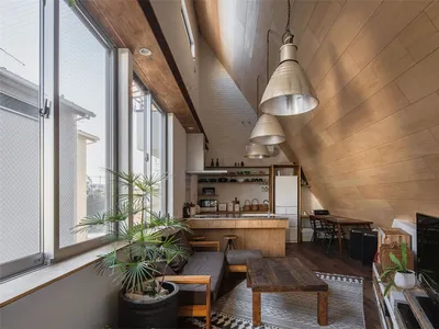 A minimalist living room and kitchen with wooden furnishings, a large window, and industrial lighting.
