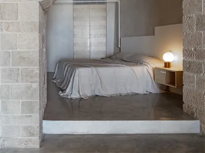 A modern minimalist bedroom featuring a concrete floor and concrete walls with an arched entryway.