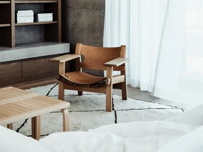 A minimalist bedroom with concrete walls, a leather chair, and a large window with white curtains.