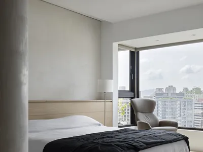 A minimalist bedroom featuring a wooden bed with a concrete headboard, black and white bedding, and a modern armchair next to