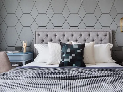 Modern bedroom featuring plush bedding on a bed with fabric headboard and hexagonal wallpaper